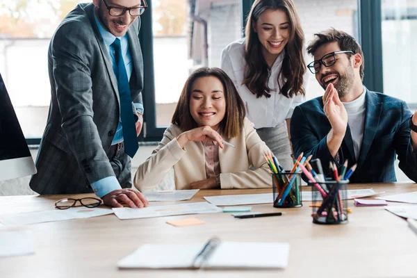 Selective focus of cheerful businessmen and happy multicultural businesswoman in office — Stock Photo