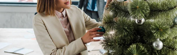Panorama-Aufnahme einer Geschäftsfrau, die in der Nähe eines geschmückten Weihnachtsbaums im Büro steht — Stockfoto
