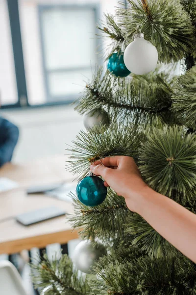 Обрізаний вид жінки, що торкається різдвяного м'яча на ялинку в офісі — стокове фото