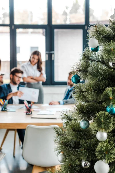 Selective focus of decorated christmas tree near coworkers in office — Stock Photo