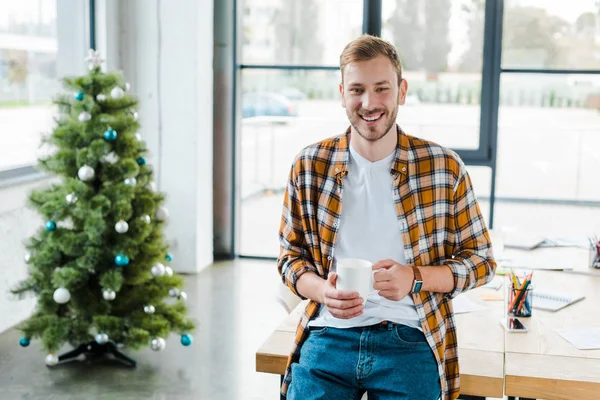 Selective focus of cheerful man holding cup near decorated christmas tree — Stock Photo