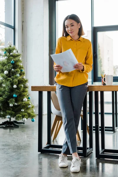 Asian businesswoman holding charts and graphs near decorated christmas tree — Stock Photo