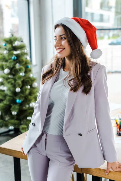 Smiling businesswoman in santa hat near christmas tree in office — Stock Photo