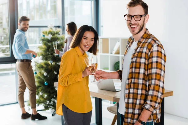 Felice donna asiatica brindare bicchieri di champagne con l'uomo vicino ai colleghi in ufficio — Foto stock