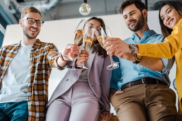 Vista angolo basso di uomini d'affari allegri e donne d'affari multiculturali brindare bicchieri di champagne in ufficio — Stock Photo