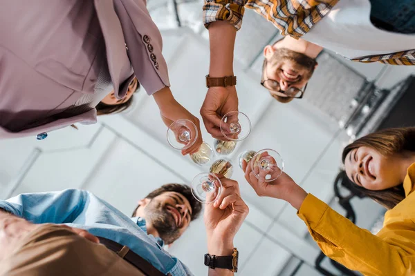 Vista dal basso di allegri uomini d'affari e donne d'affari multiculturali brindare bicchieri di champagne in ufficio — Foto stock