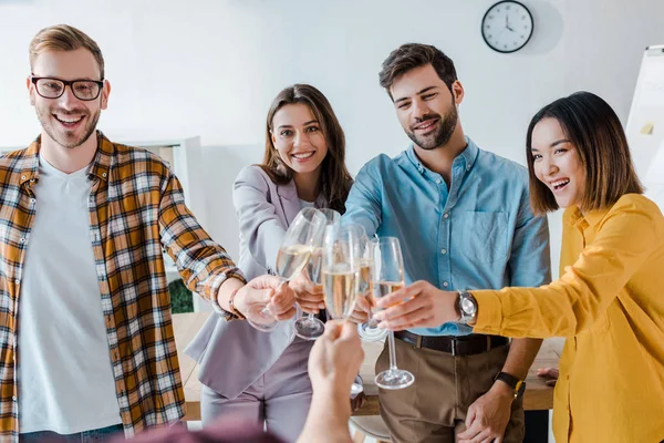 Cropped view of man toasting champagne glasses with cheerful businessmen and multicultural businesswomen in office — Stock Photo