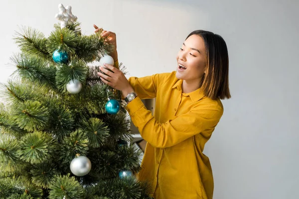 Excited asian woman decorating christmas tree in office — Stock Photo