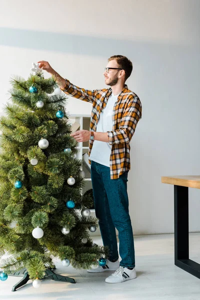 Hombre barbudo guapo en gafas decorando árbol de Navidad en la oficina - foto de stock