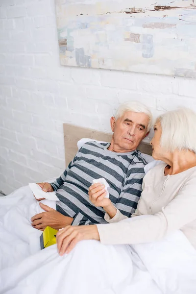 Vista ad alto angolo di marito e moglie malati che tengono i tovaglioli e parlano in appartamento — Foto stock