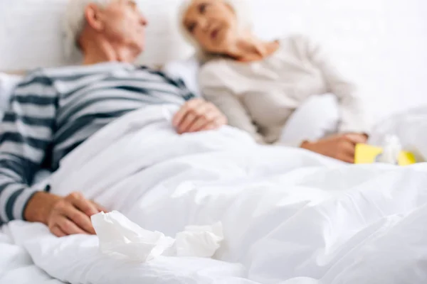 Enfoque selectivo de marido y mujer enfermos sosteniendo servilletas y hablando en el apartamento - foto de stock