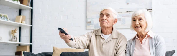 Plano panorámico de sonriente marido y mujer viendo la televisión en el apartamento - foto de stock