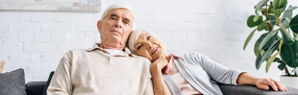 Panoramic shot of husband and smiling wife lying on shoulder and looking away in apartment — Stock Photo
