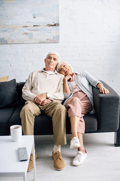Marito e moglie seduti sul divano e guardando il divano in appartamento — Foto stock
