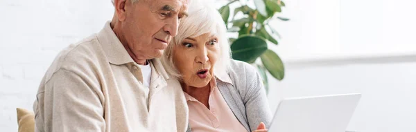 Colpo panoramico di marito e moglie scioccata utilizzando il computer portatile in appartamento — Foto stock