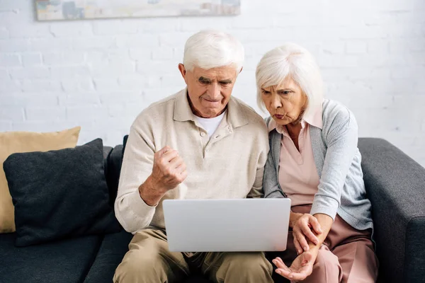 Marito mostrando sì gesto e moglie scioccata utilizzando il computer portatile in appartamento — Foto stock