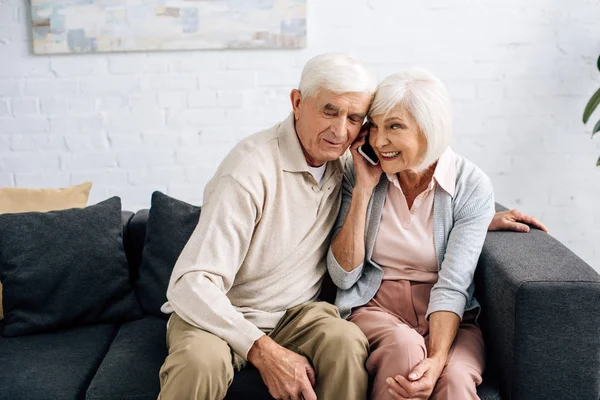 Муж и улыбающаяся жена разговаривают по смартфону в квартире — стоковое фото