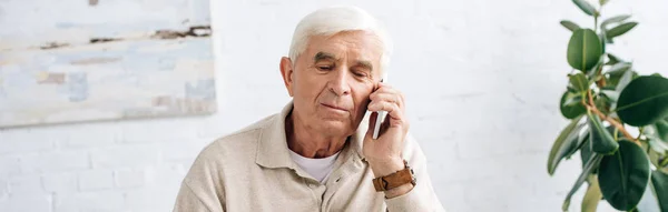 Panoramic shot of senior man talking on smartphone in apartment — Stock Photo