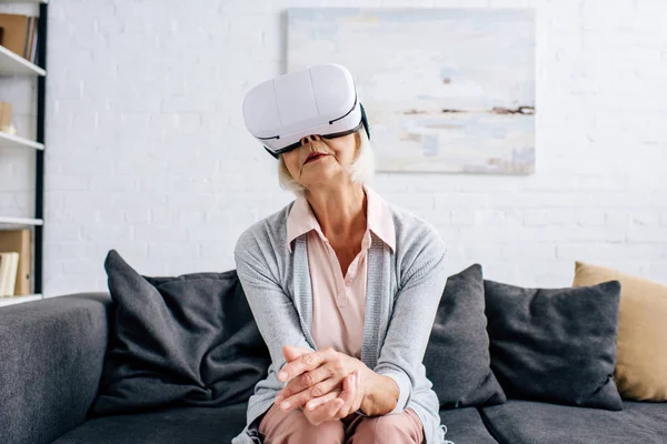 Senior woman with virtual reality headset sitting on sofa in apartment — Stock Photo