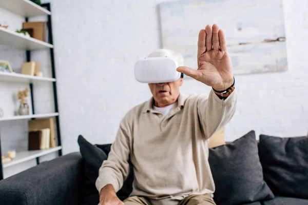 Вибірковий фокус старшого чоловіка в гарнітурі віртуальної реальності з простягнутою рукою в квартирі — стокове фото