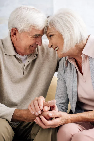 Sonriente guapo marido y atractiva esposa cogido de la mano en apartamento - foto de stock