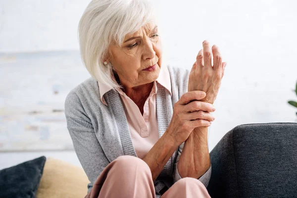 Senior woman having hand Arthritis and sitting on sofa in apartment — Stock Photo