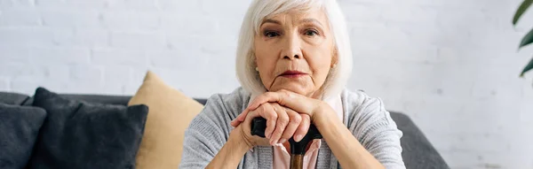 Colpo panoramico di donna anziana con canna di legno guardando la fotocamera in appartamento — Foto stock