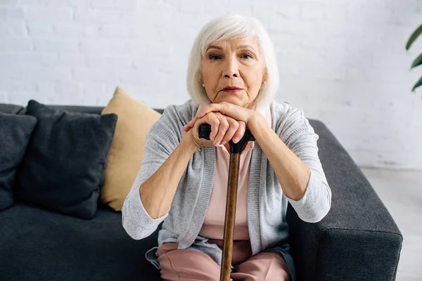 Seniorin mit Holzstock blickt in Wohnung in Kamera — Stockfoto