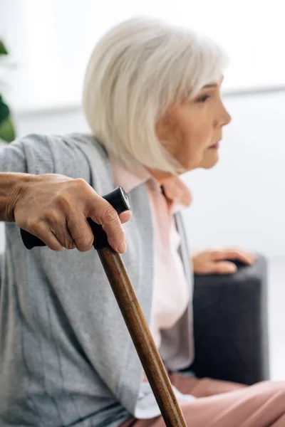 Selective focus of senior woman with wooden cane in apartment — Stock Photo