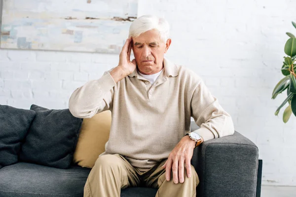 Senior man sitting on sofa and having headache in apartment — Stock Photo