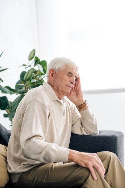 Senior man sitting on sofa and having headache in apartment — Stock Photo