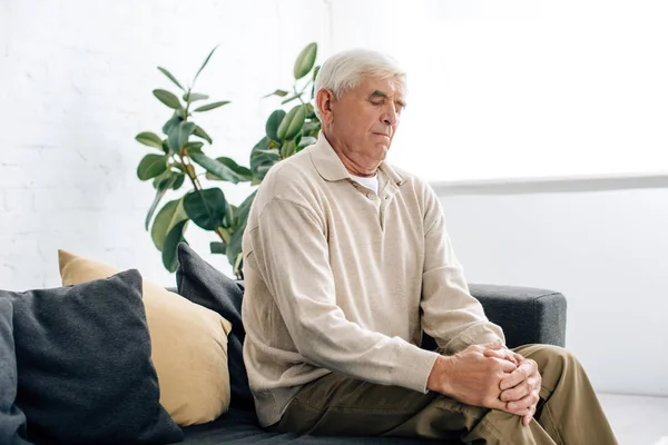 Senior man sitting on sofa and having knee Arthritis in apartment — Stock Photo