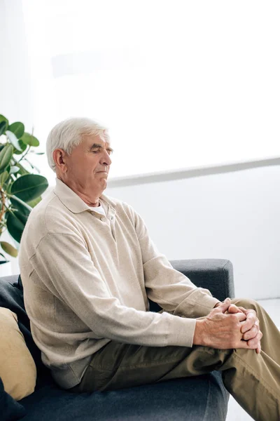 Aîné assis sur le canapé et ayant l'arthrite du genou dans l'appartement — Photo de stock