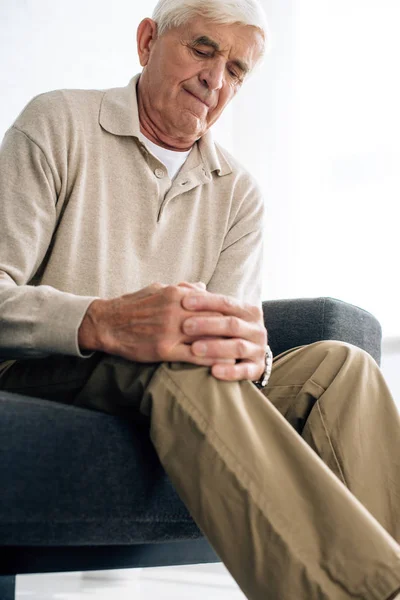 Vue de bas angle de l'homme âgé assis sur le canapé et ayant l'arthrite du genou dans l'appartement — Photo de stock