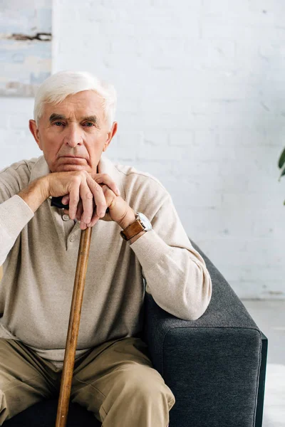 Пожилой мужчина смотрит в камеру и держит деревянную трость в квартире — стоковое фото
