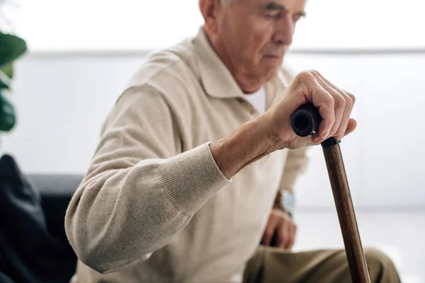 Selective focus of senior man holding wooden cane in apartment — Stock Photo