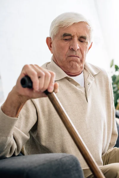 Selective focus of senior man holding wooden cane in apartment — Stock Photo