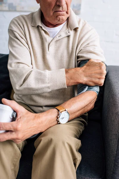 Cropped view of senior man measuring blood pressure and sitting on sofa in apartment — Stock Photo