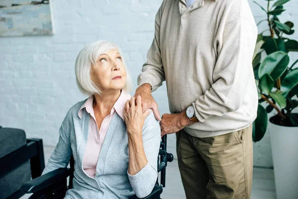 Cropped view of husband holding hand of wife in wheelchair — Stock Photo