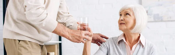 Tiro panorâmico de marido dando copo de água à esposa no apartamento — Fotografia de Stock