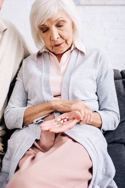 Senior woman sitting on sofa and holding pills in apartment — Stock Photo