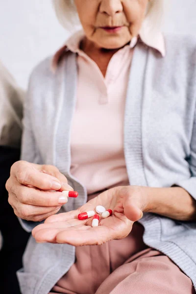 Cropped view of senior woman sitting on sofa and holding pills in apartment — Stock Photo