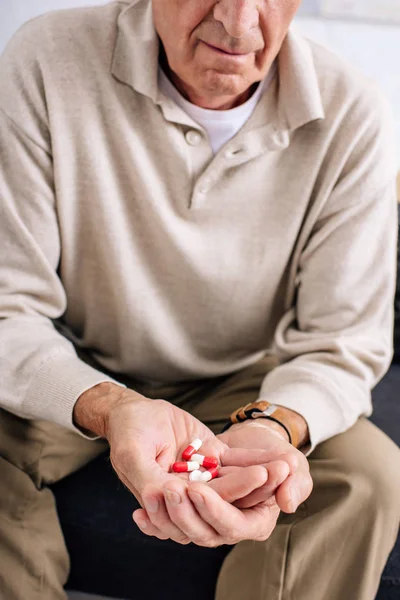 Vista recortada del hombre mayor sosteniendo píldoras en el apartamento — Stock Photo