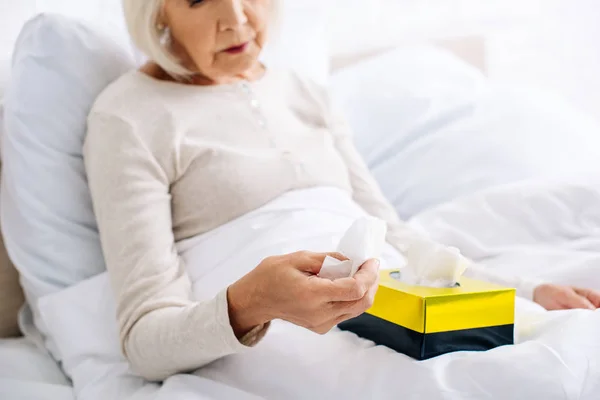 Cropped view of ill senior woman holding napkin in bed — Stock Photo