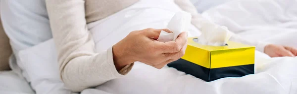 Panoramic shot of ill senior woman holding napkin in bed — Stock Photo