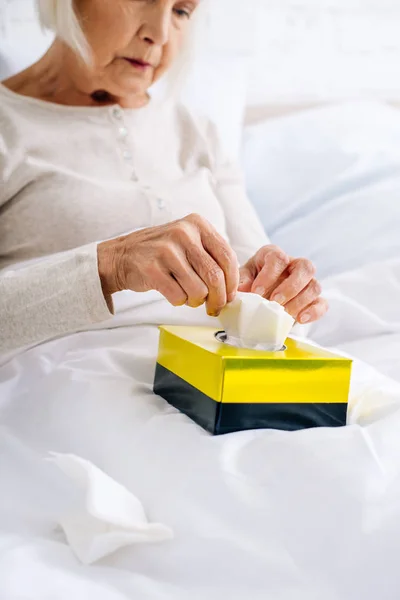 Selective focus of ill senior woman taking napkin in bed — Stock Photo
