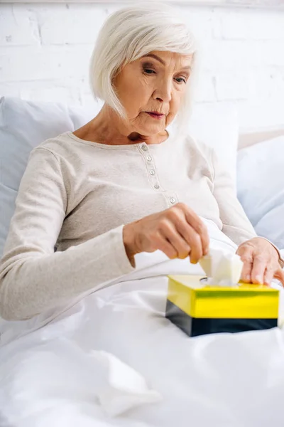 Attractive and ill senior woman taking napkin in bed — Stock Photo