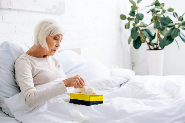 Atractiva y enferma mujer mayor tomando servilleta en la cama — Stock Photo