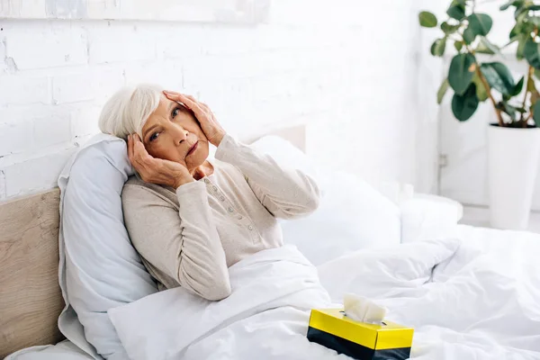 Malade femme âgée ayant mal à la tête et regardant la caméra au lit — Photo de stock