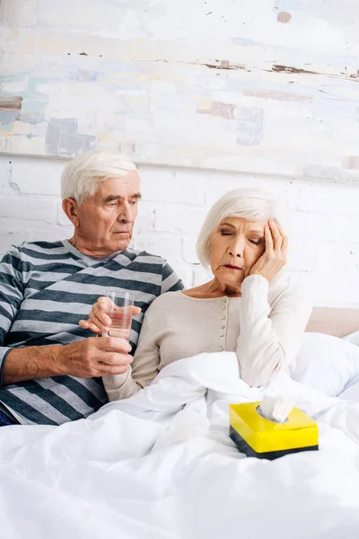 Муж дает стакан воды жене с головной болью в квартире — стоковое фото